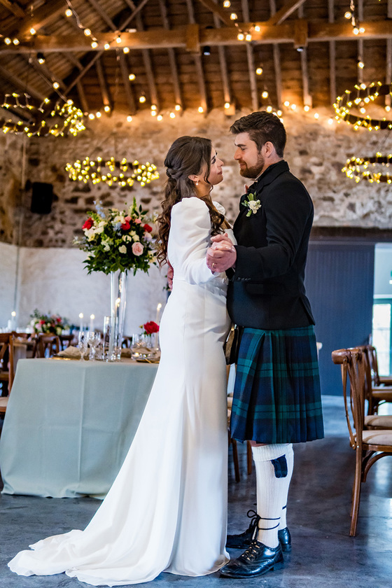 Bride and groom share a first dance in Kinclune Steading with fairy lights in background